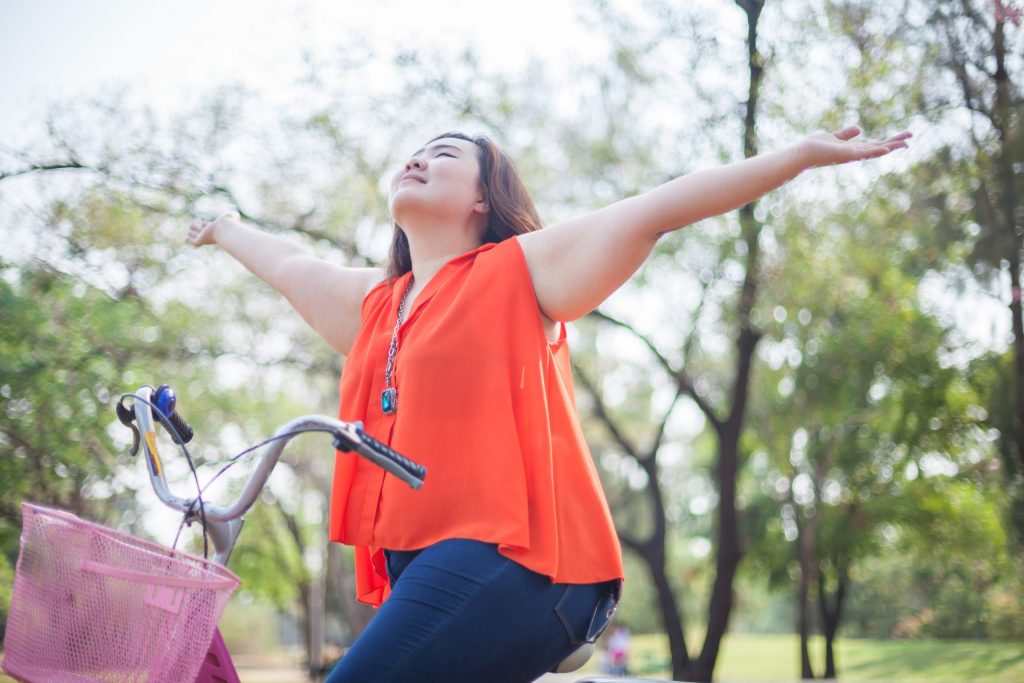 Happy fatty asian woman outstretched with bicycle outdoor in a park