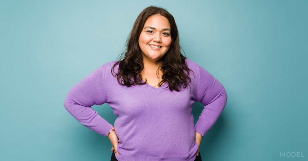 Cheerful latin woman with her hands on her hips and wearing casual clothes looking happy against a blue background (model)